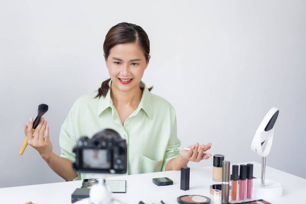 Um influenciador de beleza aplicando pó blush em sua bochecha usando pincel de maquiagem na frente de uma câmera. - Foto, Imagem