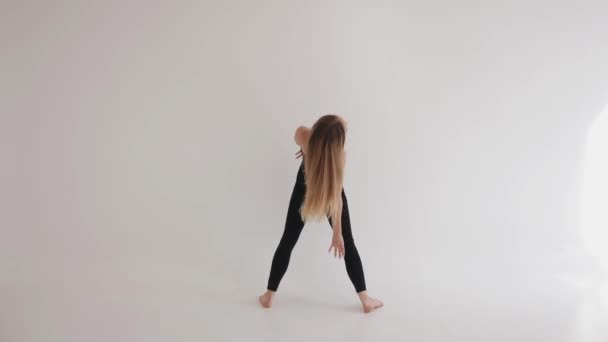 Flexible joven descalza se dedica a estirar con elementos de danza clásica en el estudio sobre un fondo blanco - Metraje, vídeo