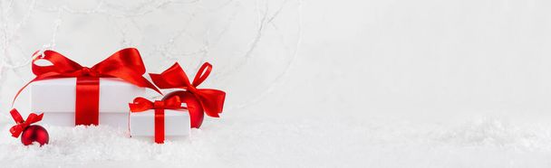 Christmas festive banner in white, red color - gift boxes with satin ribbon closeup, christmas decoration in snow under frosty white branches in winter forest, copy space. New Year background. - Foto, immagini
