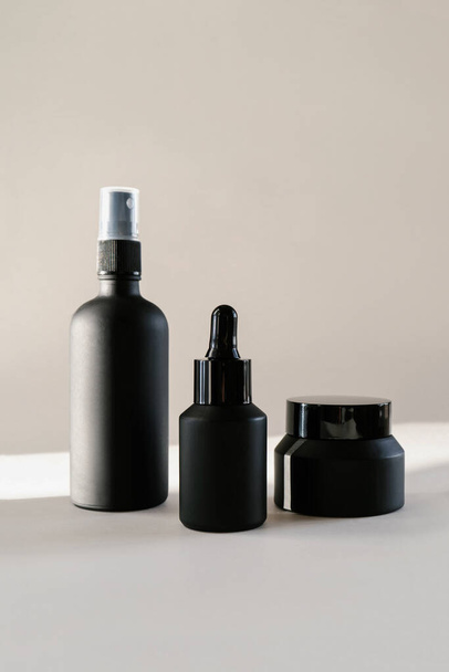 Black cosmetic bottles on a background flooded with sunlight. - 写真・画像