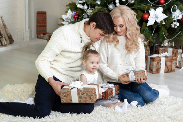 Happy young family with a child sits near a Christmas tree with gifts in their hands. On the gifts there is an inscription in Russian "Happy New Year". Portraits. Copyspase. - Photo, image
