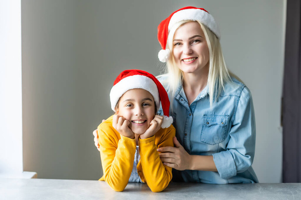 Adorable maman blonde caucasienne avec fille portant toutes les deux des casquettes de Père Noël - Photo, image