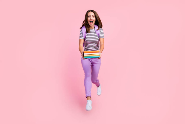 Photo of pretty impressed young woman dressed striped clothes rucksack holding diaries jumping running smiling isolated pink color background - Foto, immagini