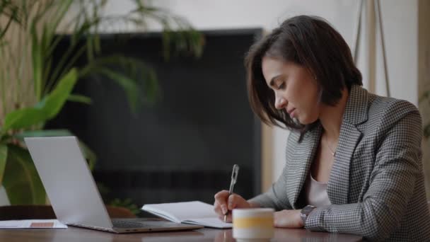 Geschäftsfrau analysiert die Grafik und tippt auf dem Laptop. Remote-Job, junge Frau mit Brille schreibt Notizen in Zwischenablage und tippt auf Laptop-Tastatur - Filmmaterial, Video