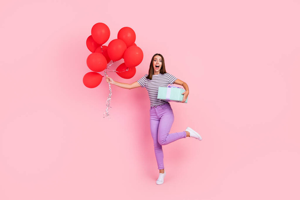 Photo of attractive excited young lady wear striped outfit smiling holding red balloons present box isolated pink color background - Foto, Imagem