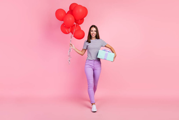 Photo of adorable shiny young woman dressed striped clothes holding many red balloons gift box smiling isolated pink color background - Фото, зображення