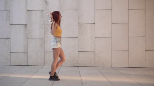 Bella donna attiva sta camminando con uno skateboard all'aperto. Donna rossa sportiva adolescente per strada. Stile di vita giovanile - Filmati, video