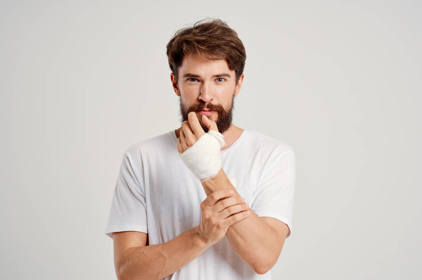 męski pacjent w białej koszulce z bandażowaną dłonią pozującą na szpitalną medycynę - Zdjęcie, obraz
