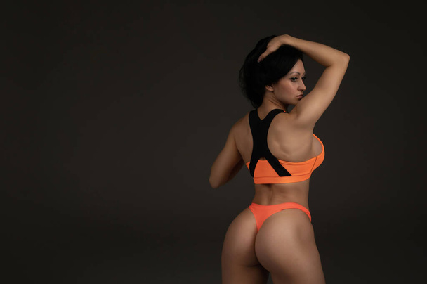 back view of attractive slim fit woman in orange sportswear posing on grey background - Fotoğraf, Görsel
