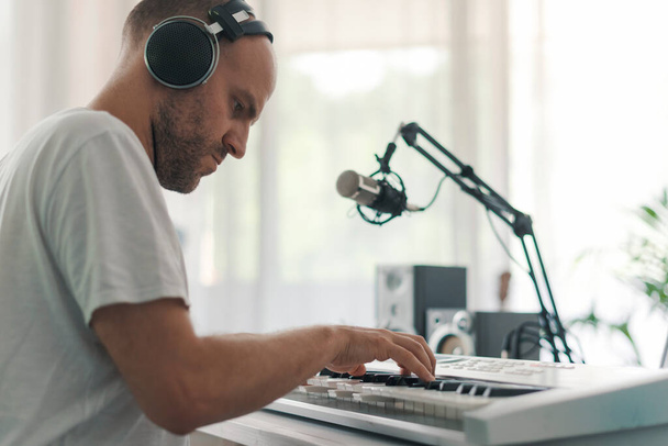 Professional musician composing music at home, he is wearing headphones and playing a digital piano - Zdjęcie, obraz