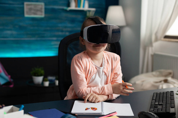 Children experiencing virtual reality using headset while sitting at desk table - Photo, Image