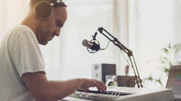 Professional musician composing music at home, he is wearing headphones and playing a digital piano - 写真・画像
