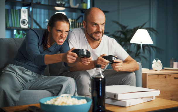 Paar sitzt auf der Couch zu Hause und spielt Videospiele zusammen, sie halten den Controller und konzentrieren sich auf das Spiel - Foto, Bild