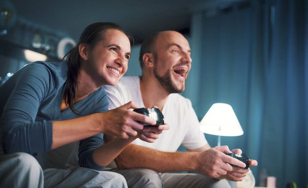 Happy couple spending their weekend at home, they are sitting on the couch and playing video games - Photo, Image