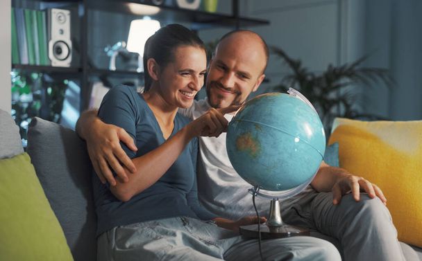 Happy couple picking a destination on the globe for their next travel - Fotó, kép
