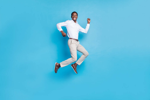 Photo of lucky pretty dark skin guy dressed formal shirt humping high rising fist smiling isolated blue color background - Foto, afbeelding