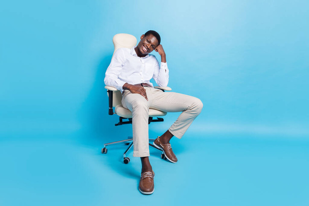 Photo of pretty thoughtful dark skin guy dressed formal shirt sitting chair smiling isolated blue color background - Фото, зображення