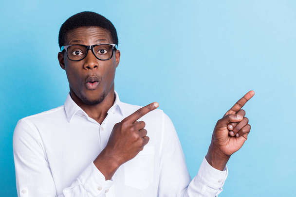 Photo of impressed shocked dark skin man wear white shirt spectacles pointing empty space isolated blue color background - Zdjęcie, obraz