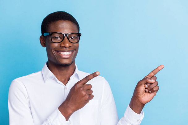 Photo of cute charming dark skin guy dressed formal shirt glasses smiling pointing empty space isolated blue color background - Φωτογραφία, εικόνα