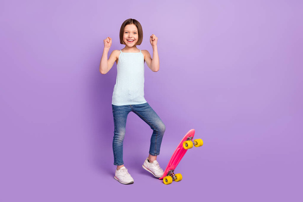 Foto de cuerpo completo de alegre feliz niña pequeña agradable levantar puños patinador ganador aislado sobre fondo de color púrpura - Foto, imagen