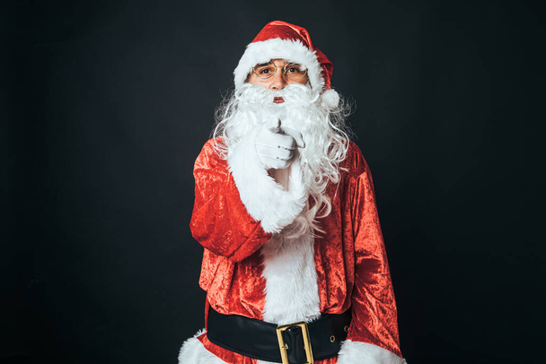 Άνδρας ντυμένος Άγιος Βασίλης με το δάχτυλο στραμμένο στην κάμερα, σε μαύρο φόντο. Χριστούγεννα έννοια, Άγιος Βασίλης, δώρα, γιορτή. - Φωτογραφία, εικόνα