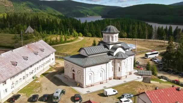Légi drón kilátás az Oasa kolostorra Romániában. Templomok, parkoló autók, Kárpátok, erdõvel borított hegyek, tó - Felvétel, videó