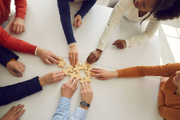 Multiracial office workers assembling wooden puzzles on desk symbolizing development and success. - Foto, Imagen