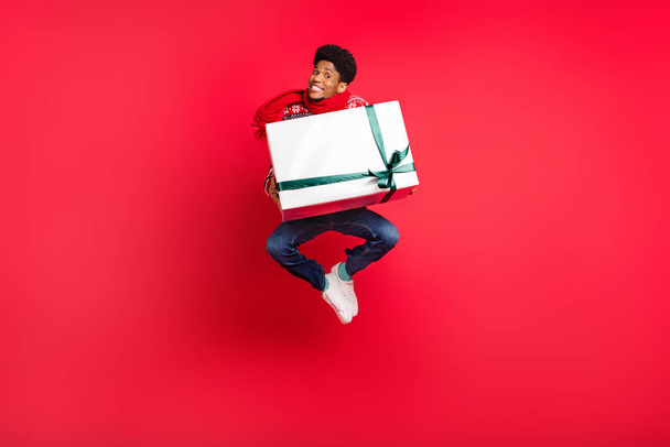 Full length photo of young afro guy happy positive smile jump gift holiday spirit new year isolated over red color background - Photo, Image