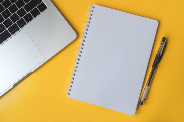 Escritorio amarillo con portátil y bloc de notas con pluma. Página de cuaderno en blanco para texto - Foto, imagen