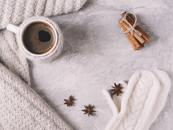 Una fredda mattina d'inverno e una tazza di caffè in un maglione su un tavolo di pietra bianca con cannella, una sciarpa lavorata a maglia e guanti caldi - Foto, immagini