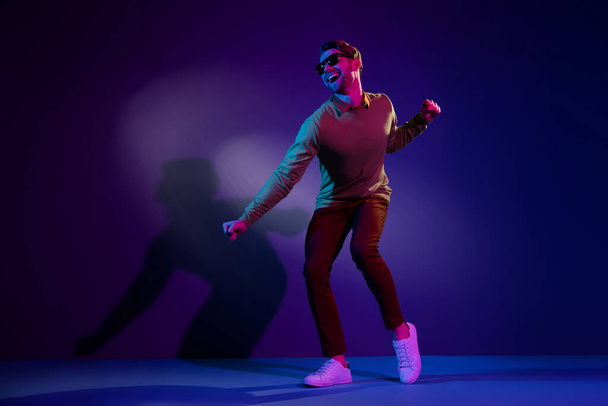Volledige lengte foto van jonge chill guy dans dragen brillen trui broek geïsoleerd op blauwe kleur achtergrond - Foto, afbeelding
