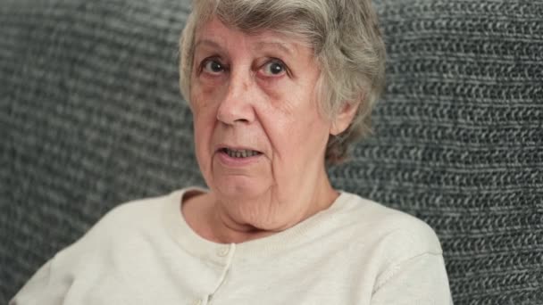 Old woman speaks emotionally sitting on couch in living room - Footage, Video