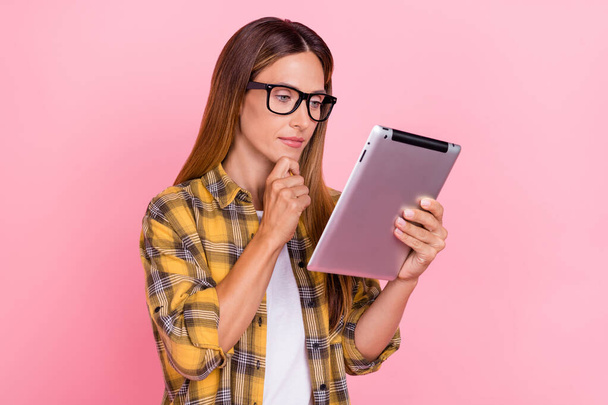 Foto van ernstige gerichte vrouw houd handen tablet slijtage bril denken minded geïsoleerd op roze kleur achtergrond - Foto, afbeelding