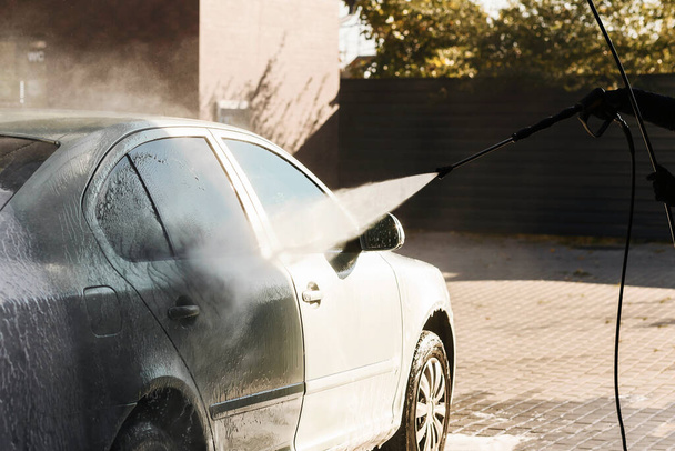 Auto pesee voimakkaan vedenpaineen alla letkusta automaattisella pesualtaalla, taustavalolla, ulkona. Puhdistus auton käsite. - Valokuva, kuva