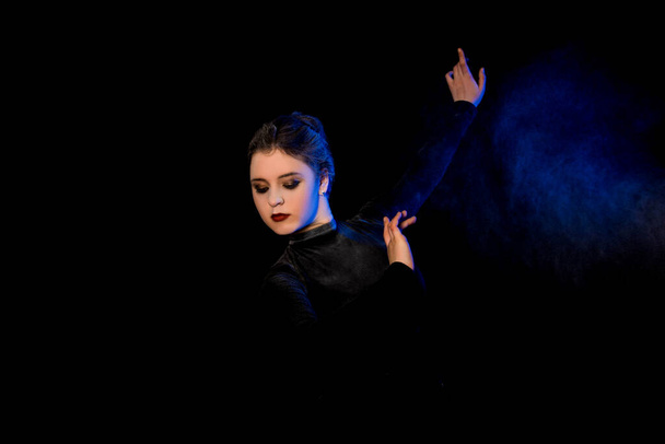 Junge schöne Ballerina posiert im Studio. Schöne schlanke Tänzerin im schwarzen Kleid. Blauer und lila Rauch Hintergrund. Künstlerin und Turnerin. - Foto, Bild