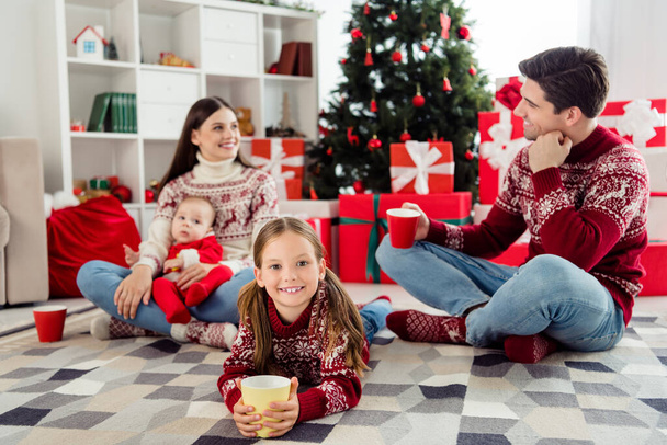 Photo of funny dreamy couple two kids dressed new year pullovers smiling talking drinking beverages indoors house home room - 写真・画像