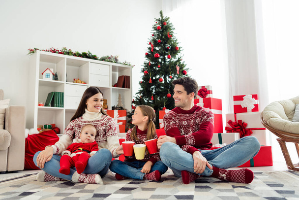 Foto von glänzenden süßen großen Familie tragen Weihnachtspullover sitzen unter Baum trinken heißen Tee lächelnd drinnen Zimmer zu Hause Haus - Foto, Bild