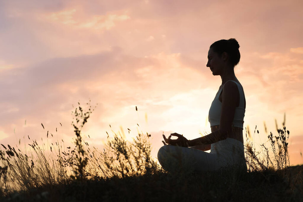 Mature woman meditating outdoors at sunset. Space for text - 写真・画像
