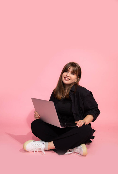  Student brown haired Girl in casual clothes Holding Laptop Computer Sitting On Pink Background. Online Education Concept. Studio Shot. Looking at camera - Photo, image