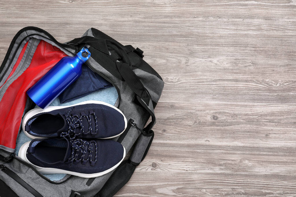 Grey gym bag with sports stuff on wooden  background, top view. Space for text - 写真・画像