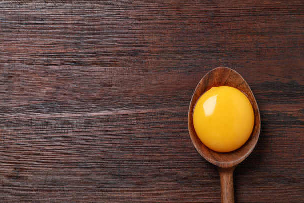 Spoon with raw egg yolk on wooden table, top view. Space for text - Foto, Bild