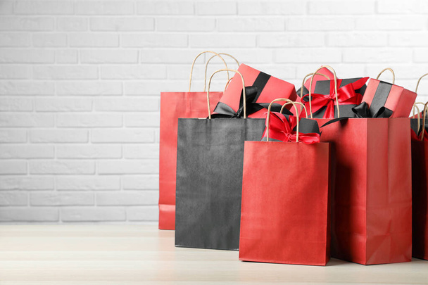 Paper shopping bags and gift boxes on table near white brick wall, space for text. Black Friday sale - Fotoğraf, Görsel