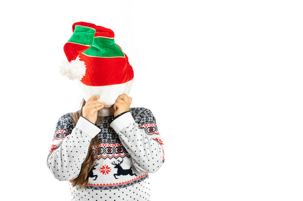 child in white knitted Christmas sweater with reindeer hide face under dwarf hat, isolated on white background - Photo, image