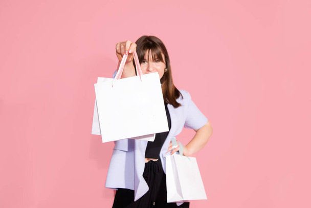photo of lovely young woman in casual clothing is happy with gift bags, shopping for spring holiday on pink background in studio. Celebrating Woman's Day, birthday, Valentine's, anniversary. Copy space, blank - Valokuva, kuva