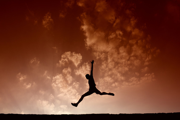 Силуэт спортсмена, прыгающего с голубым небом и облаками на спине
 - Фото, изображение