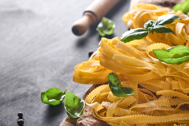 Tagliatelle. Homemade pasta, basil leaves, flour, pepper, olive oil, cherry tomato and rolling pin and pasta knife on dark old wooden background. Food concept. Mock up. Horizontal with copy space. - Foto, Bild