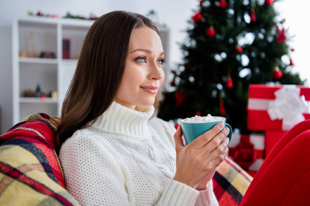 Photo of pretty charming young woman dressed knitted sweater drinking cocoa smiling indoors room home house - Foto, afbeelding