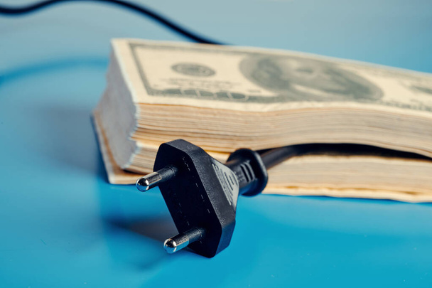 ηλεκτρικό καλώδιο που προκύπτει από μια στοίβα τραπεζογραμματίων δολαρίων, το οποίο απεικονίζει την υψηλή τιμή της ηλεκτρικής ενέργειας - Φωτογραφία, εικόνα