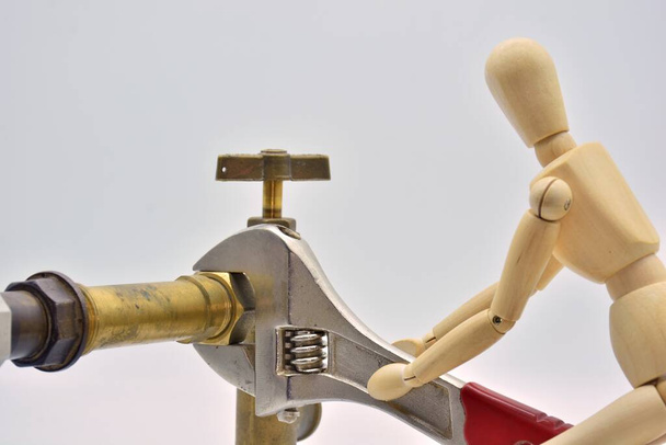 Ξύλινη κούκλα με ρυθμιζόμενο κλειδί, σφίγγοντας ένα παξιμάδι υδραυλικών, απομονωμένη σε λευκό φόντο - Φωτογραφία, εικόνα