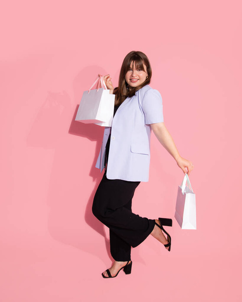 Full length photo of lovely young woman in casual clothing is happy with gift bags, shopping for spring holiday on pink background in studio. Celebrating Woman's Day, birthday, Valentine's, anniversary. - Photo, Image